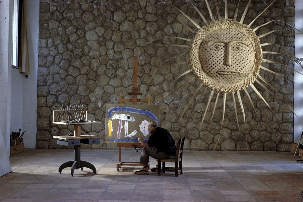 Joan MIRO peignant un tableau dans son atelier de MAJORQUE avec un énorme soleil de palmes tressées pendu à une ficelle.