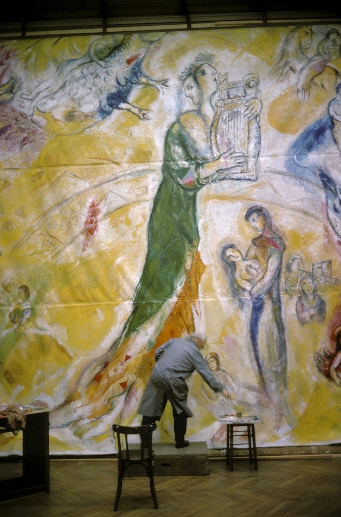 Le peintre Marc CHAGALL de dos, en blouse grise, debout sur une petite estrade, peignant un des panneaux qui décorera le plafond de la coupole du Palais Garnier à PARIS.